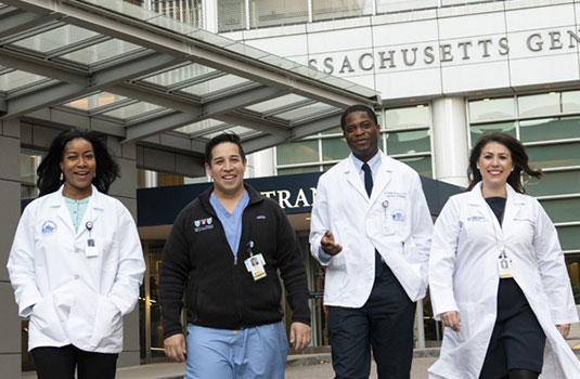 Four clinicians walking in front of Mass General main entrance